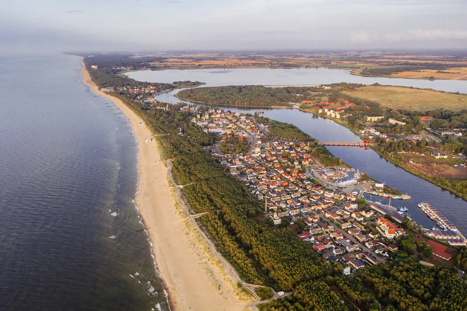 Widok z lotu ptaka na szeroką piaszczystą plażę w Dziwnowie, morze i zabudowę miasta nad rzeką Dziwną